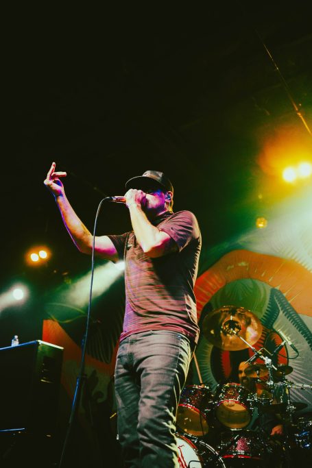 Male singer performing on stage with a microphone, colorful lights in the background.